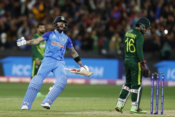 Cricketer wearing blue uniform and helmet screams in joy next to a dejected-looking man wearing green.